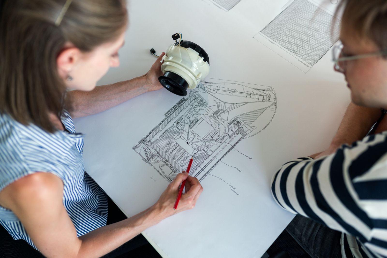 Patent-style technical drawings spread on a drafting table beside the physical part they depict.