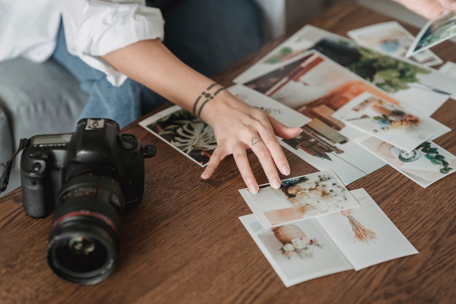 A photographer reviewing her own printed photographs on a wooden table, camera beside them.