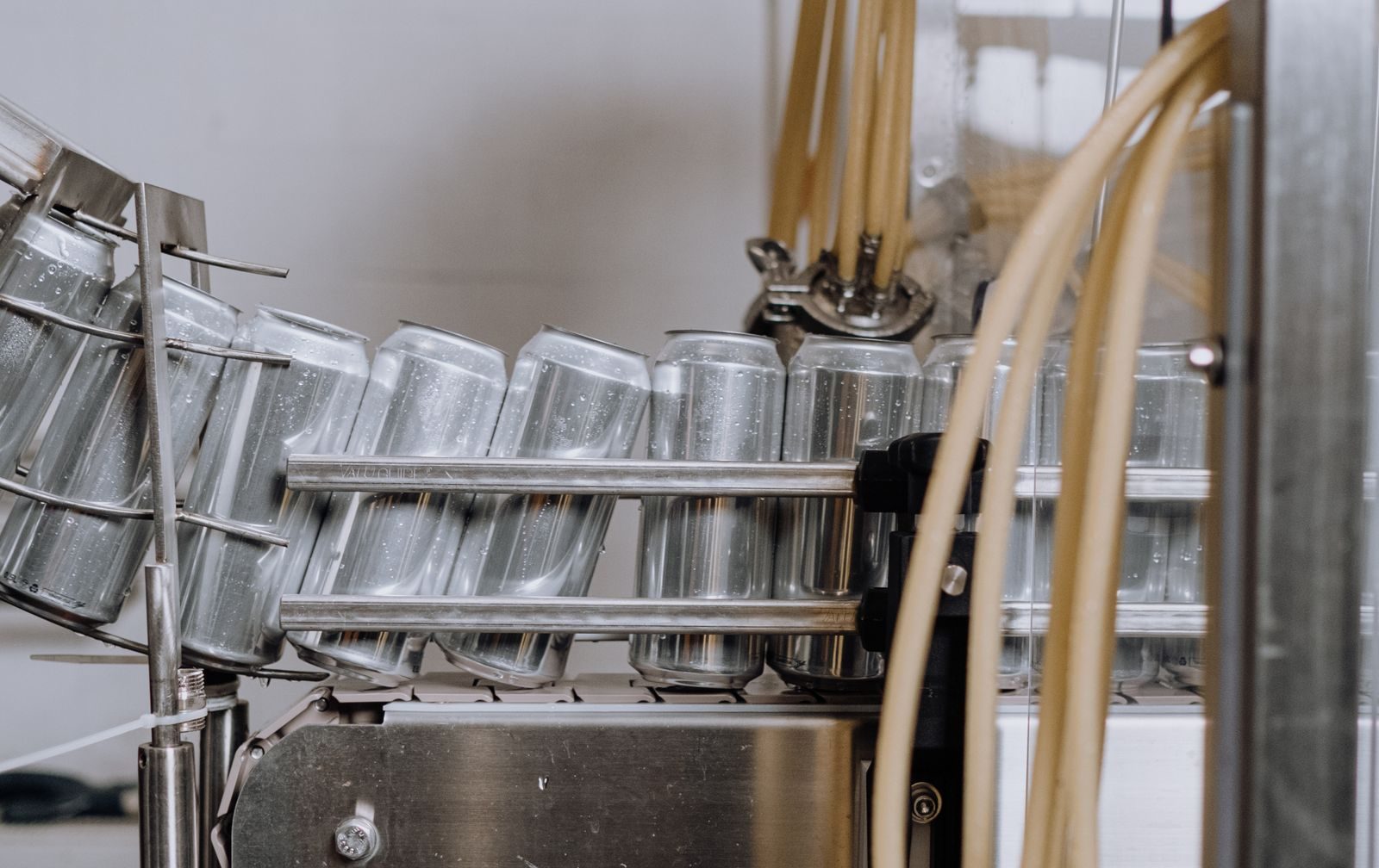 Unlabeled aluminum cans moving along a beverage-factory canning line.